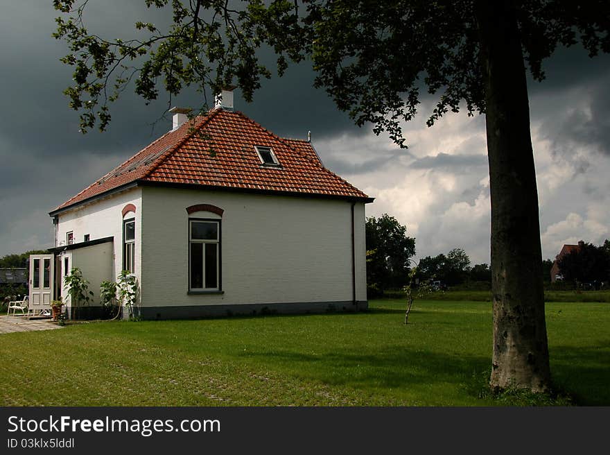 Authentic Dutch white house in the countryside with dark rain clouds on the background. Authentic Dutch white house in the countryside with dark rain clouds on the background