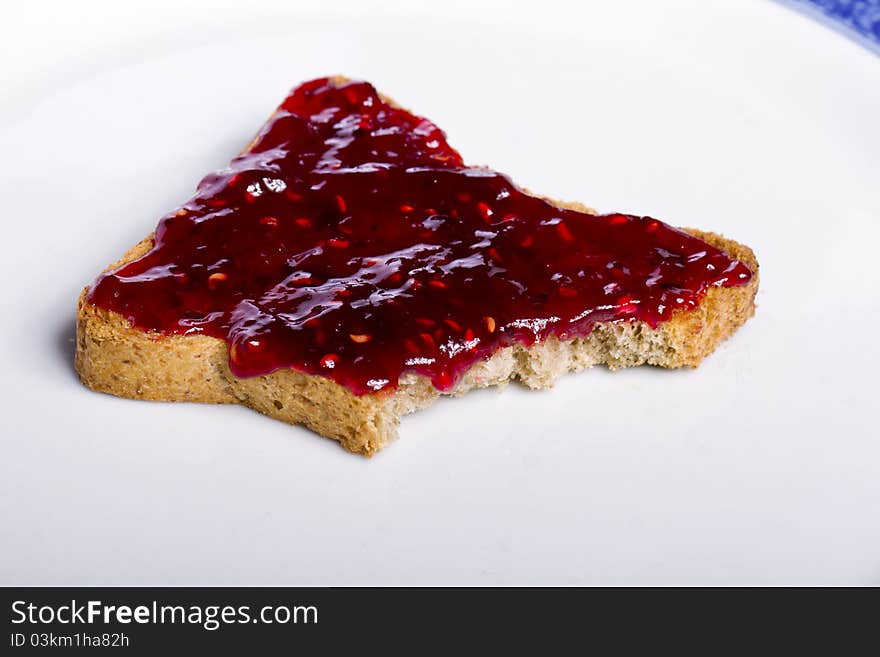 Close view of a toasted bread with berry jam spread on a white background. Close view of a toasted bread with berry jam spread on a white background.