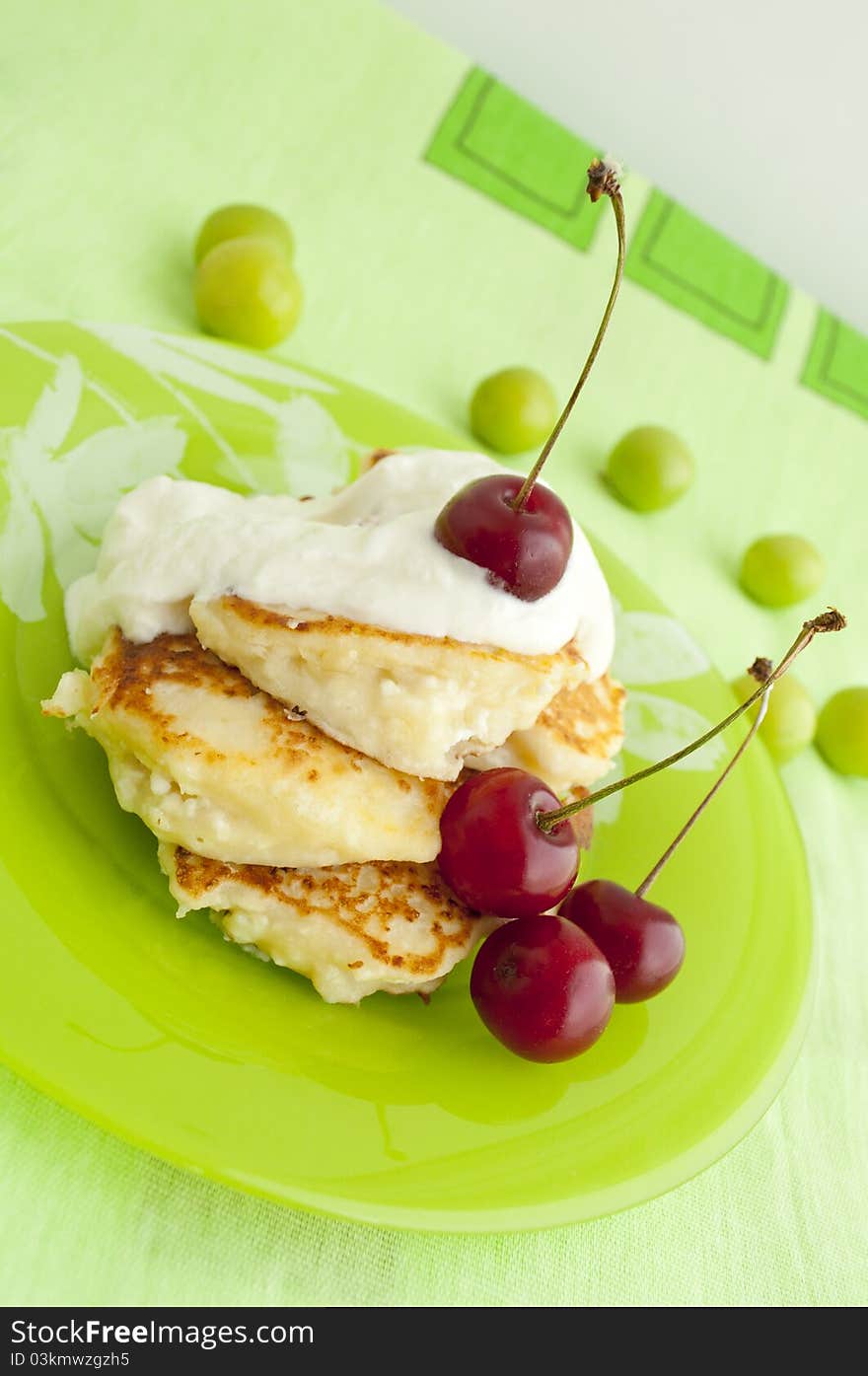 Pancakes with cherries and cream on green plate