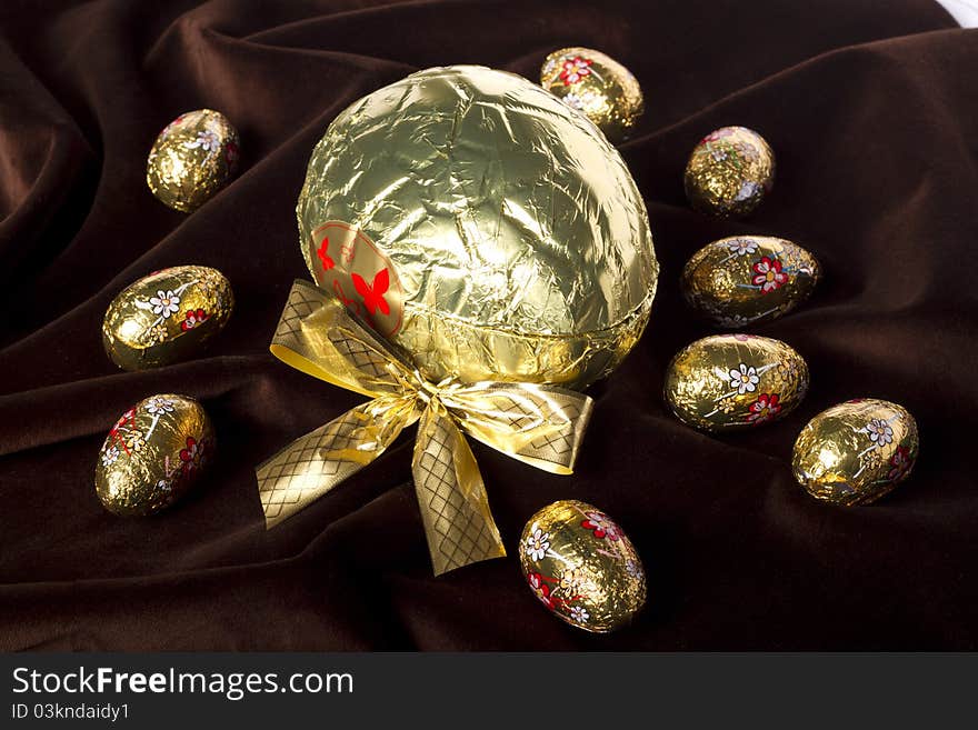 Close up view of sweet golden eggs of chocolate spread on a dark brown silk background. Close up view of sweet golden eggs of chocolate spread on a dark brown silk background.