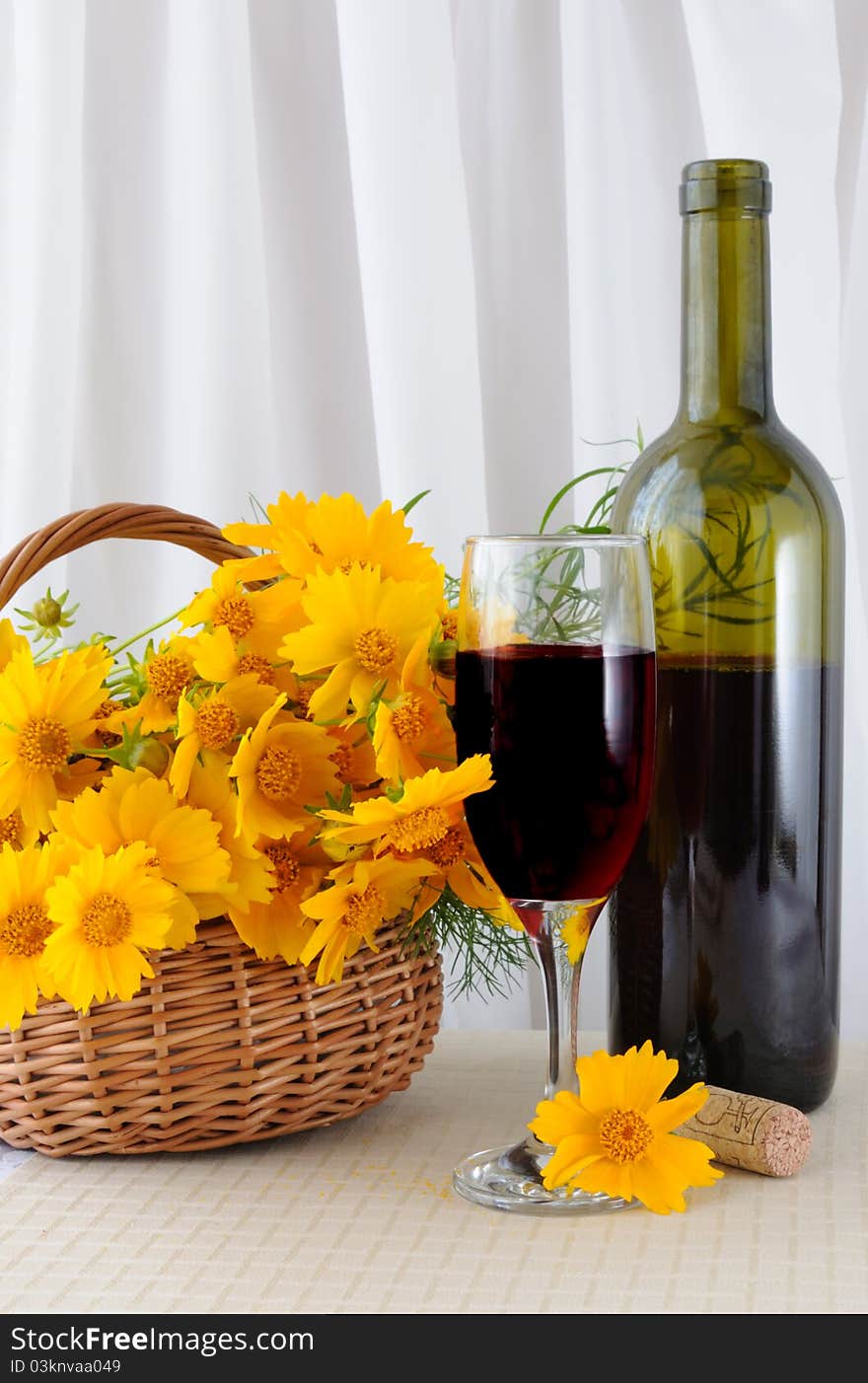 A glass of rose wine with an open bottle and yellow flowers in a basket. A glass of rose wine with an open bottle and yellow flowers in a basket