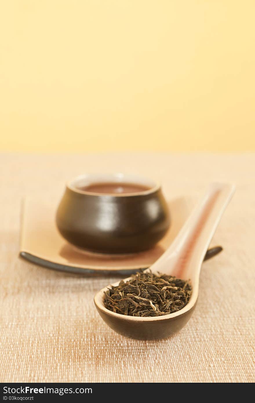 Black tea on ceramic spoon, tea in tea bowl in background. Traditional tea still life. Black tea on ceramic spoon, tea in tea bowl in background. Traditional tea still life.