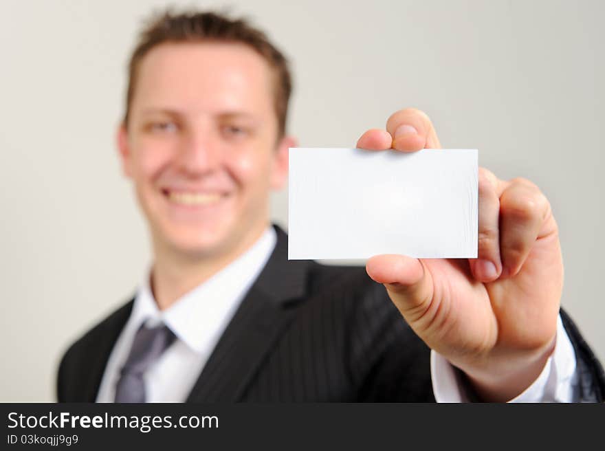 Ambitious white man in business suit smiles confidently and holds out his business card; selective focus on card. Ambitious white man in business suit smiles confidently and holds out his business card; selective focus on card