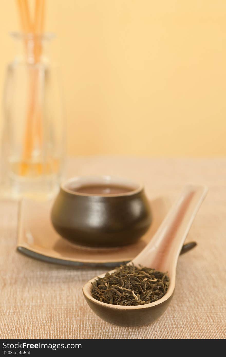 Black tea leaves on spoon, tea in tea bowl in background. Black tea leaves on spoon, tea in tea bowl in background.