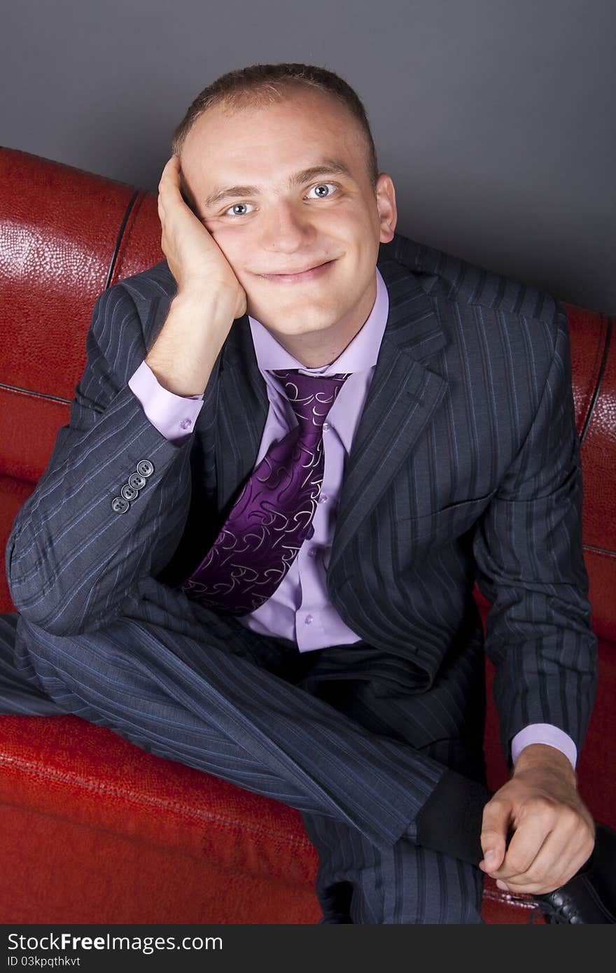 Thoughtful young man in a suit sitting on a red couch. Thoughtful young man in a suit sitting on a red couch