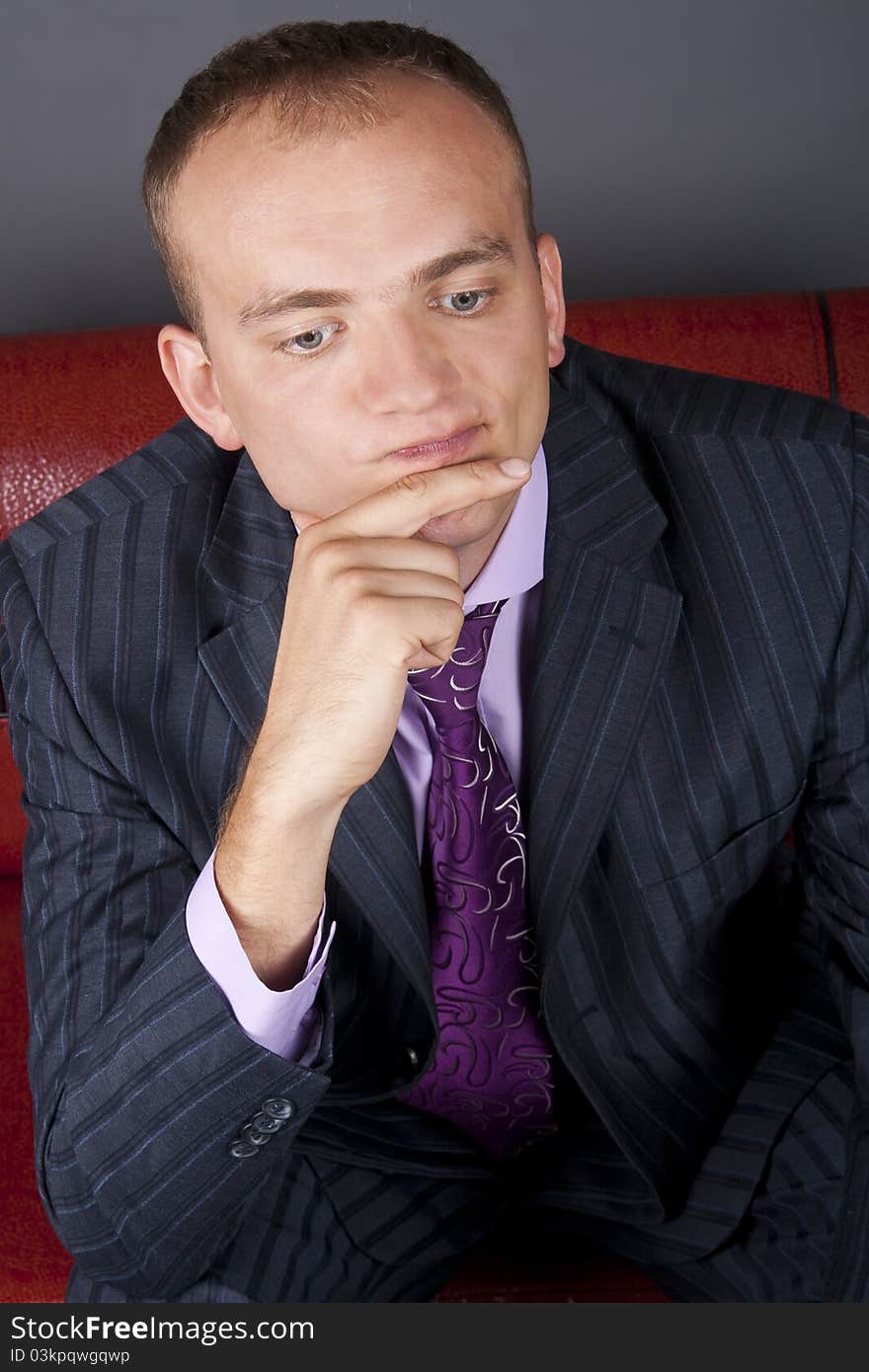 Thoughtful guy in a suit sitting on a red couch