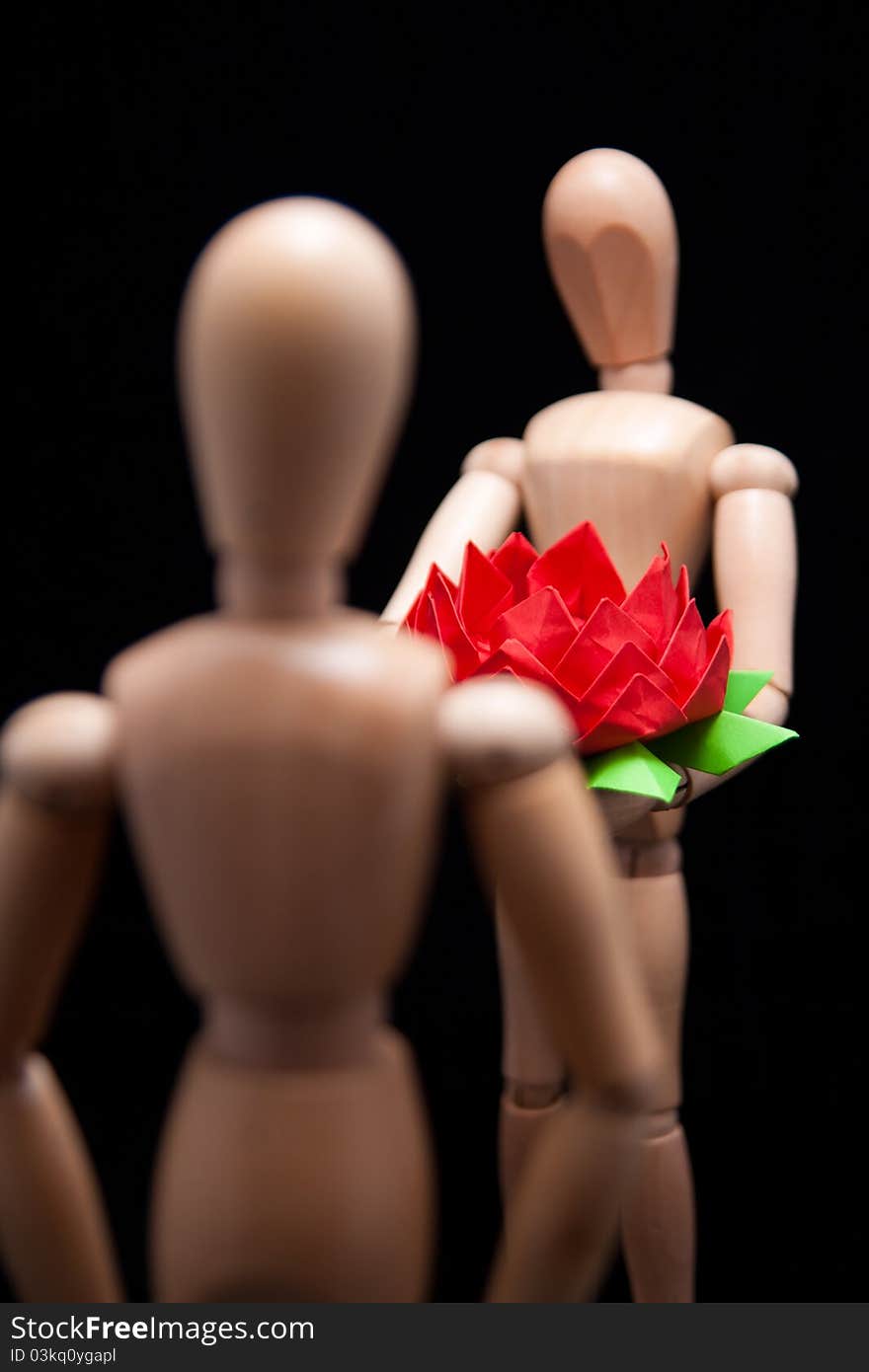 A wooden mannequin giving hand-made paper flower to another mannequin. Shallow DOF, focus is on the flower. This photo made over black background but is not isolated. A wooden mannequin giving hand-made paper flower to another mannequin. Shallow DOF, focus is on the flower. This photo made over black background but is not isolated.