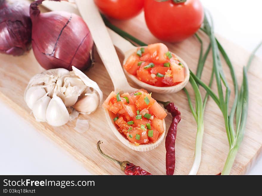 Salsa in two spoons on a wooden board and the ingredients: tomatoes, onions, garlic, chili pepper. Salsa in two spoons on a wooden board and the ingredients: tomatoes, onions, garlic, chili pepper