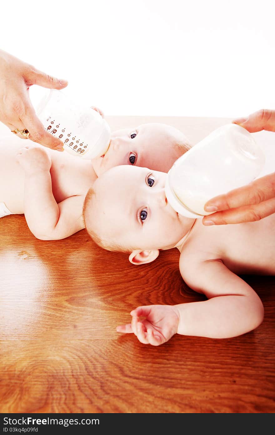 Baby twins drinking milk from bottle holding by their parents