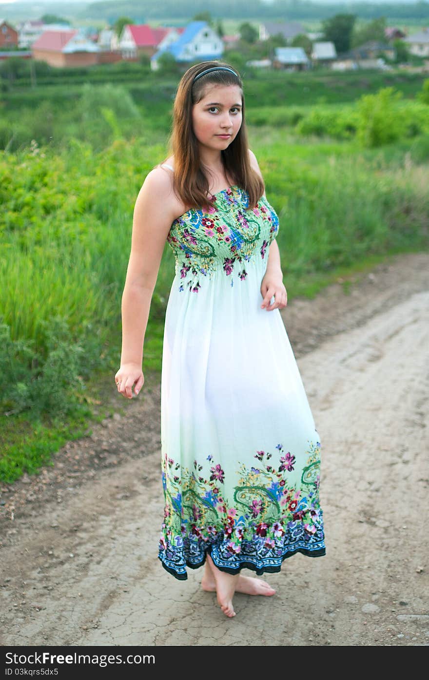 The portrait of young smiling girl in light dress on the road