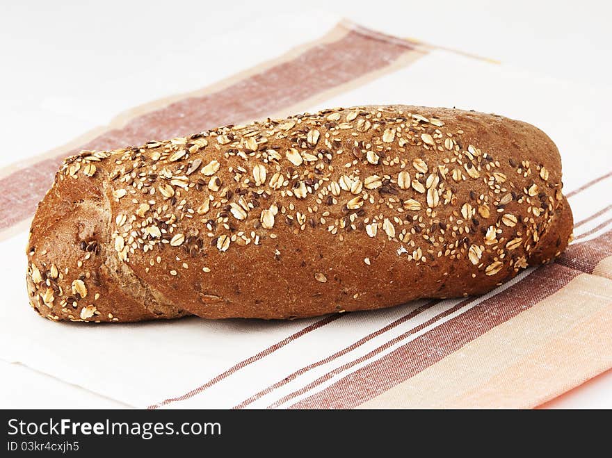 Long loaf of rye bread strewed by sunflower seeds on a white background