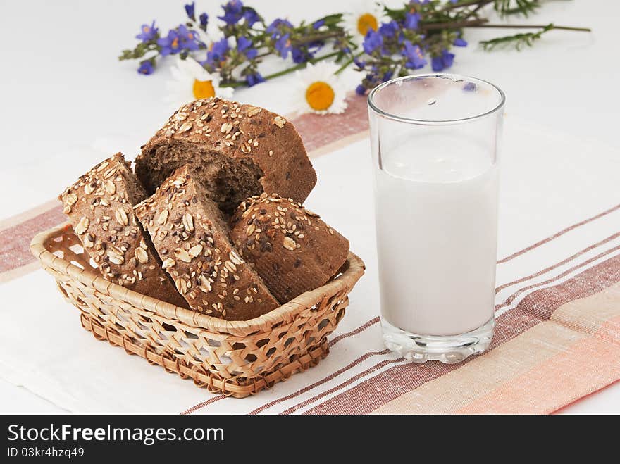 Summer Breakfast. The cut black bread in a basket, a glass of milk and a small summer bouquet on a linen towel. Summer Breakfast. The cut black bread in a basket, a glass of milk and a small summer bouquet on a linen towel