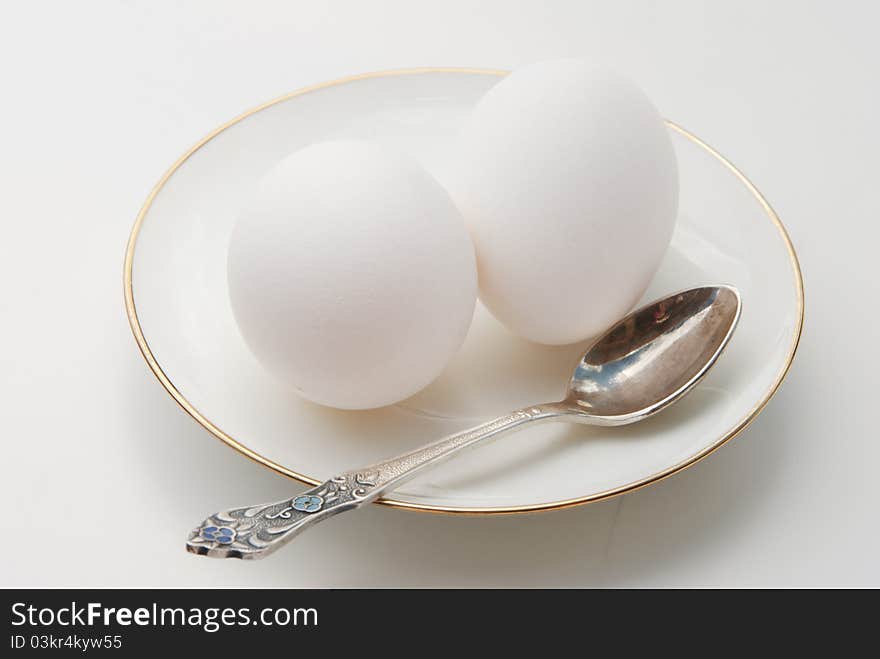 Breakfast. Two white eggs on a white plateau and a spoon on a light background. Breakfast. Two white eggs on a white plateau and a spoon on a light background