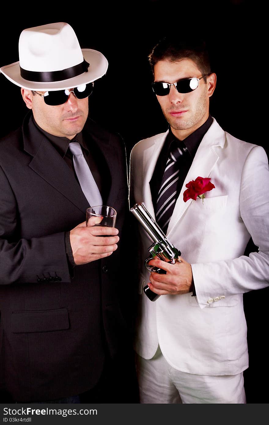 View of two gangster males holding a gun on a black background. View of two gangster males holding a gun on a black background.