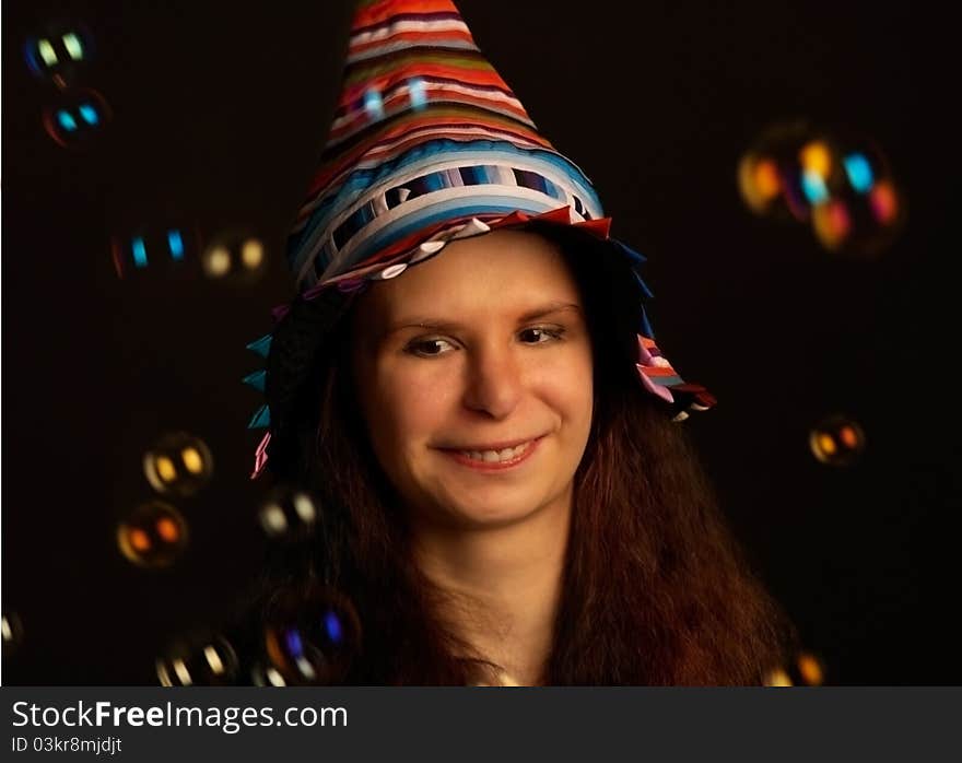 Studio portrait of happy young woman in fool's cap. Soap bubbles are around. Studio portrait of happy young woman in fool's cap. Soap bubbles are around