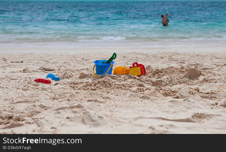 Beach toys on a tropical beach with a father and son swimming in the ocean on the background