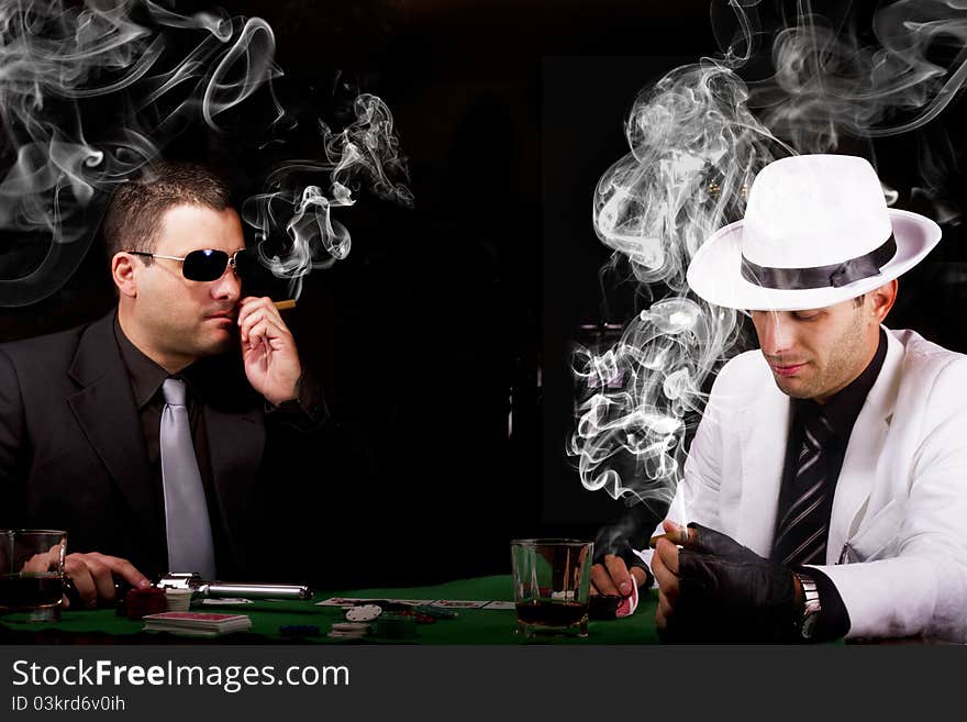 View of two gangster males playing some poker and smoking Cuban cigars. View of two gangster males playing some poker and smoking Cuban cigars.