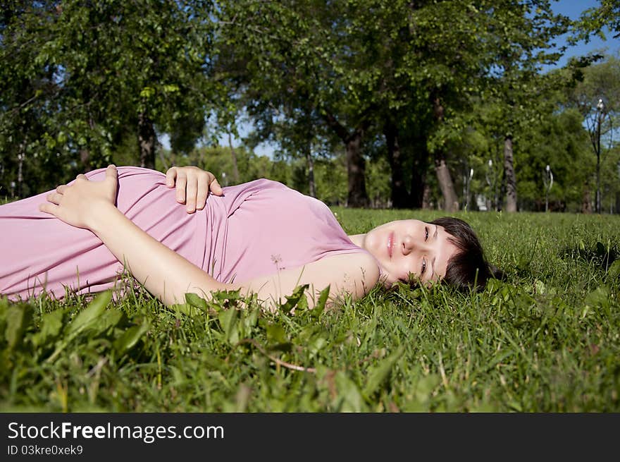 The young pregnant girl in park, has a rest on a grass. The young pregnant girl in park, has a rest on a grass