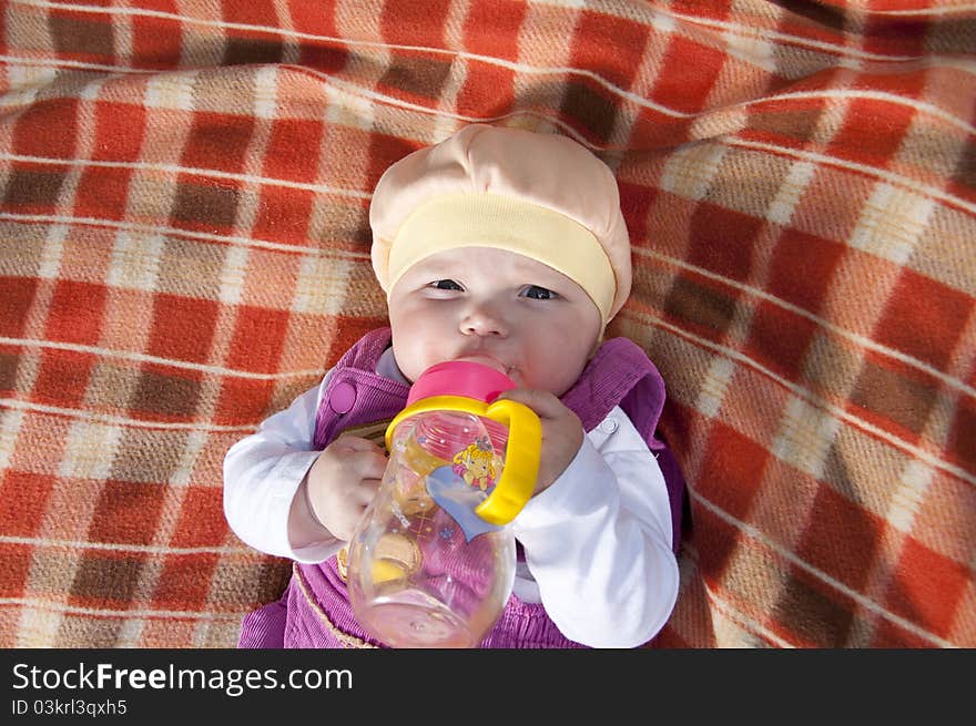 The portrait of the kid, lays on on a coverlet and drink water