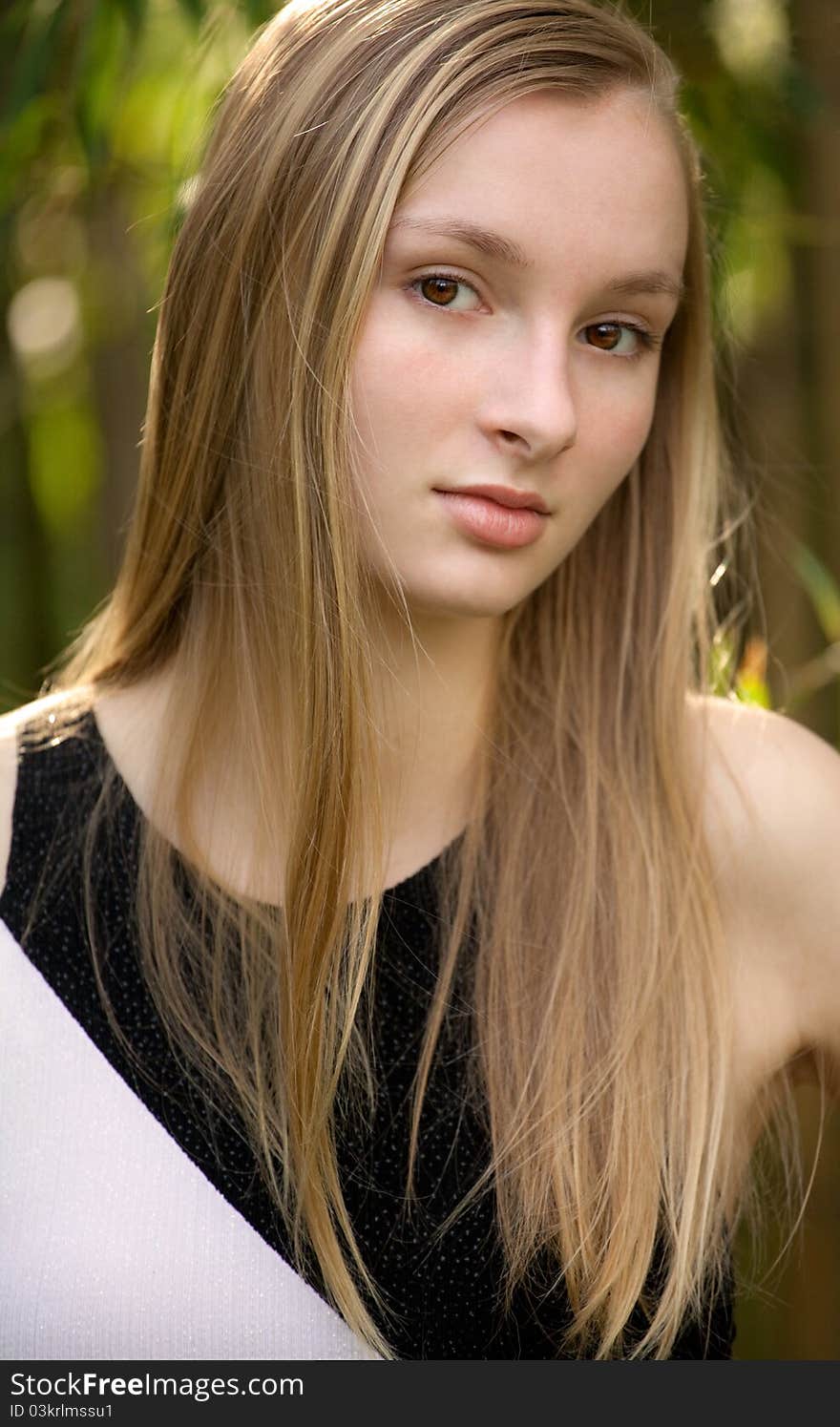 A portrait of a teenager making eye contact with the viewer, with trees in the background. A portrait of a teenager making eye contact with the viewer, with trees in the background