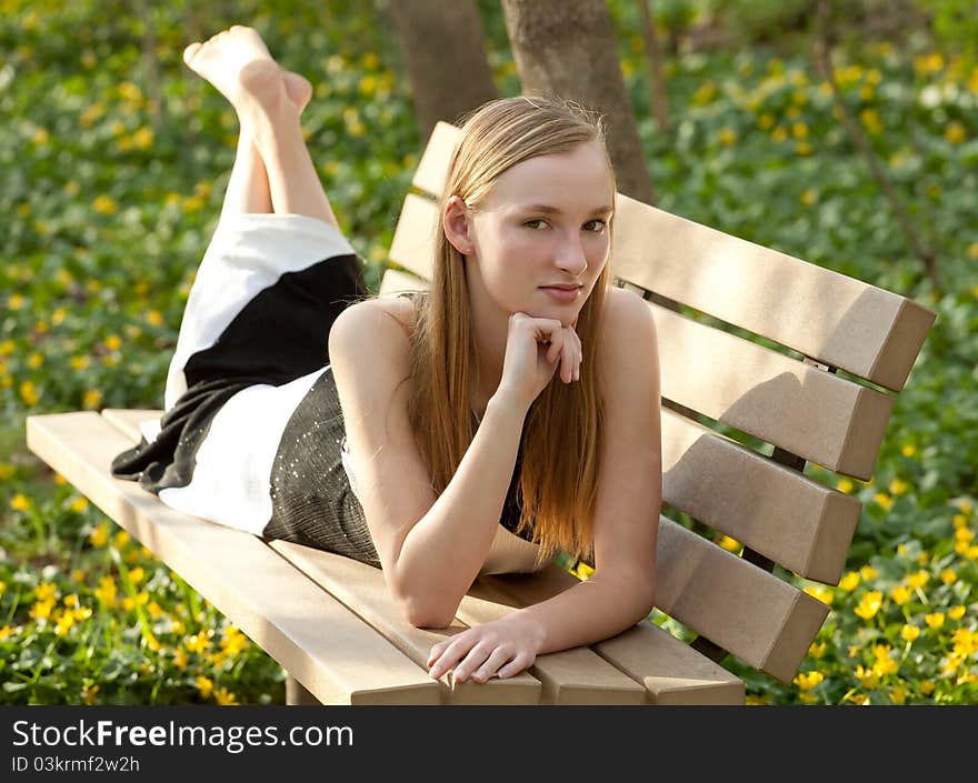 A portrait of a beautiful teenage girl lying on a park bench in a gorgeous dress, surrounded by flowers. A portrait of a beautiful teenage girl lying on a park bench in a gorgeous dress, surrounded by flowers