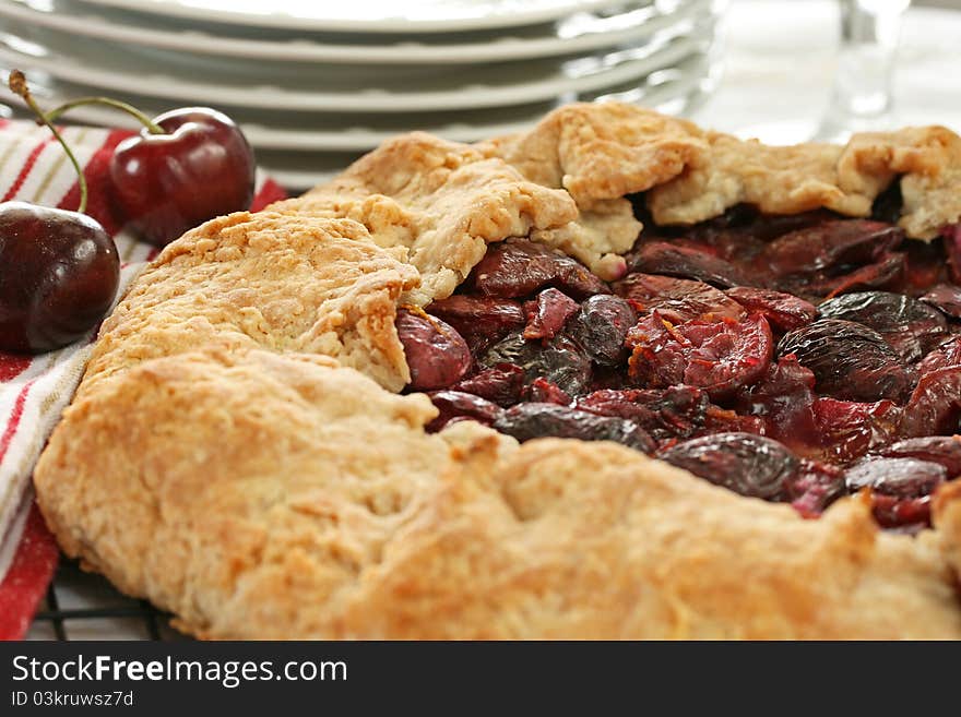 Fresh cherry crostata with two cherries, dishes and water glass in background. Fresh cherry crostata with two cherries, dishes and water glass in background