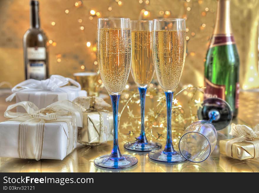 Champagne in glasses,gift boxes,bottles of wine on gold background with twinkle lights. Champagne in glasses,gift boxes,bottles of wine on gold background with twinkle lights.