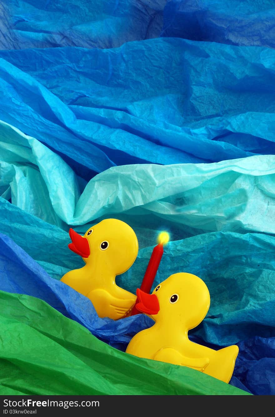 2 yellow ducks with a red candle on a blue aqua and green background. 2 yellow ducks with a red candle on a blue aqua and green background