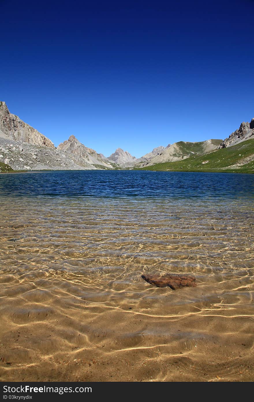 Translucent lake of mountain with some sand and a rock in foreground. Translucent lake of mountain with some sand and a rock in foreground.