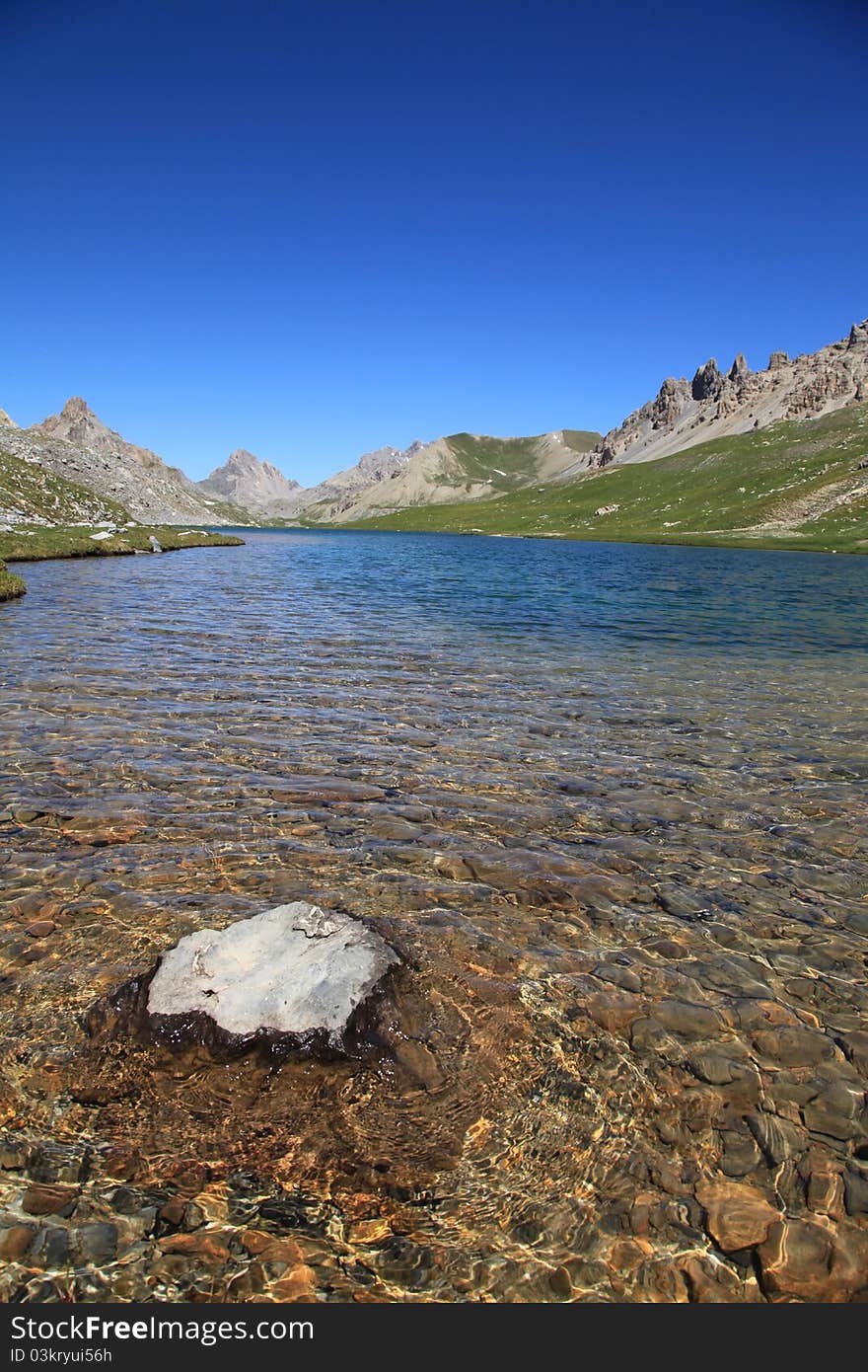 A translucent lake in mountains with a rock in foreground. A translucent lake in mountains with a rock in foreground.