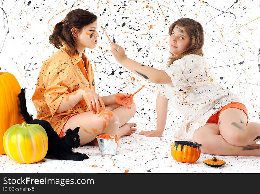 Two sisters deep in black and orange paint, surrounded by pumpkins, a black can and a paint-spattered background. Two sisters deep in black and orange paint, surrounded by pumpkins, a black can and a paint-spattered background.