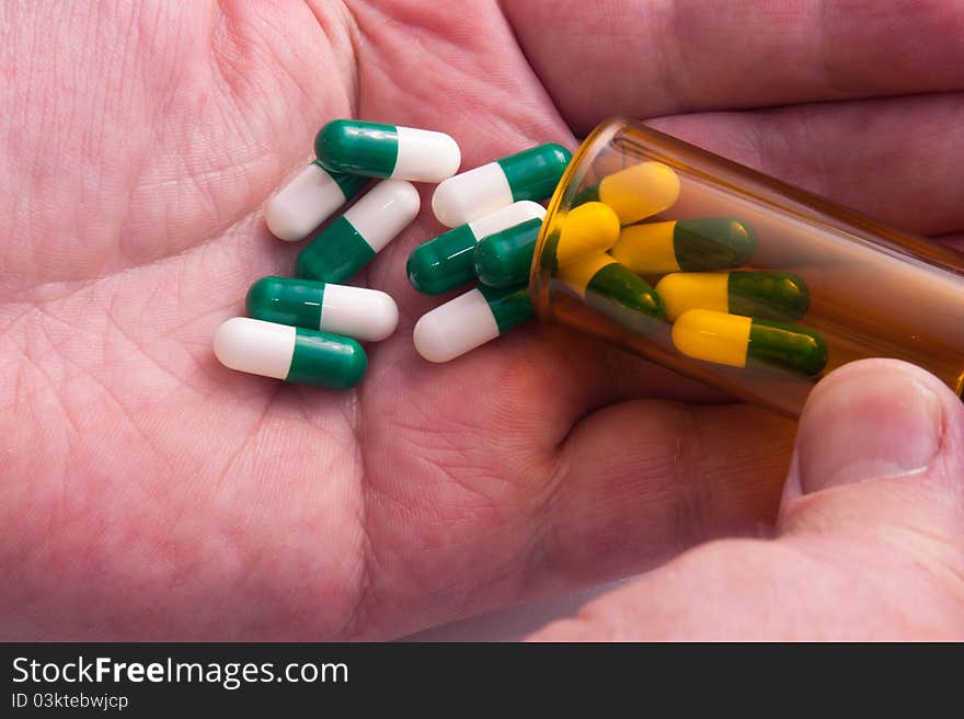 Pill Containers with Green and White capsules inside, poured on a male hand. Pill Containers with Green and White capsules inside, poured on a male hand