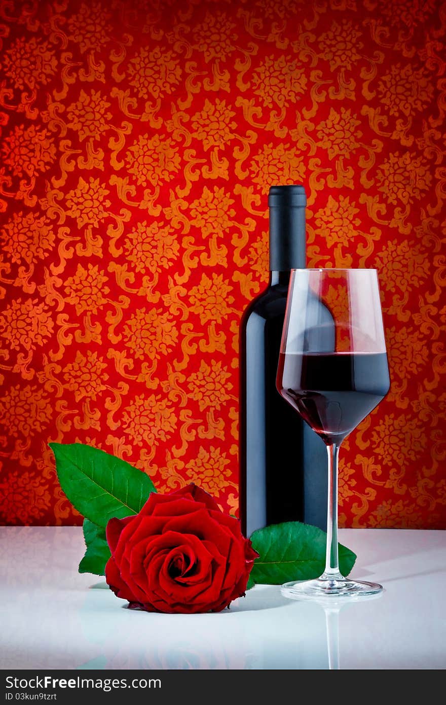 Bottle of red wine with half filled wine glass and beautiful red rose on patterned red background. Bottle of red wine with half filled wine glass and beautiful red rose on patterned red background