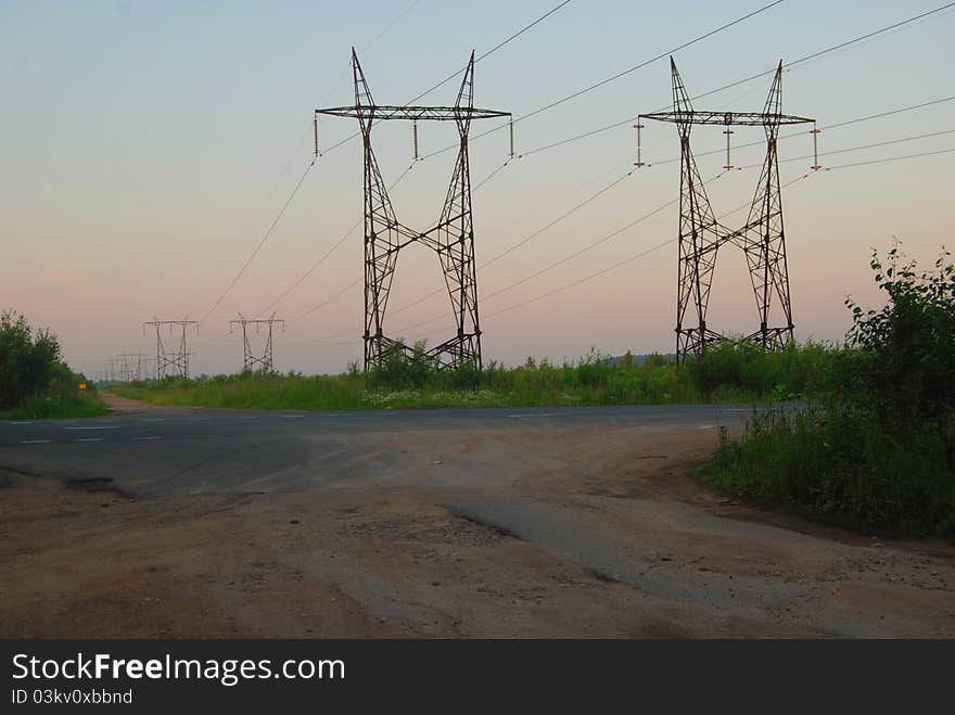 Landscape with high-voltage line over the asphalted road. Warm evening light and clear sky