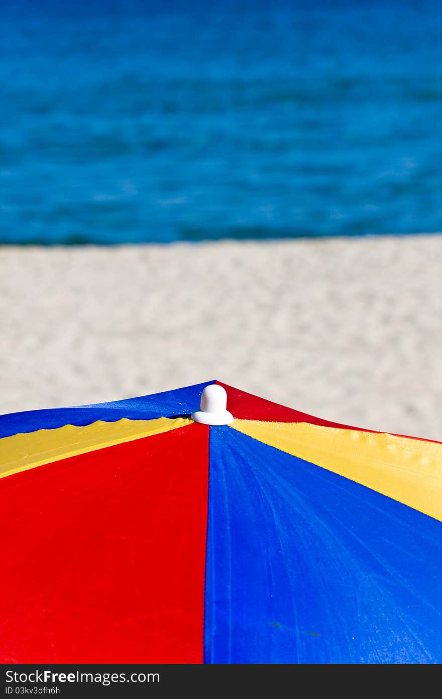 Colorful beach umbrella with white beach and blue sea background