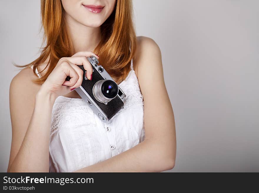 Redhead girl in white dress with vintage camera. Studio shot.