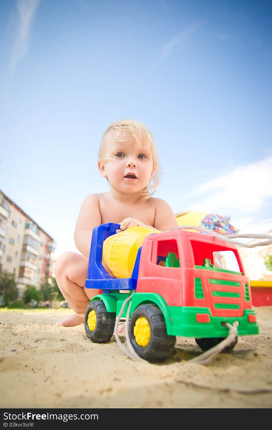 Adorable baby play with toy concrete mixer truck on playground on sand