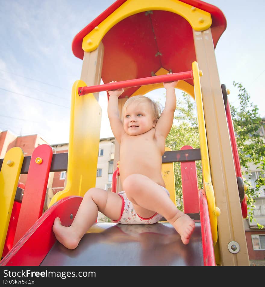 Young adorable baby sliding down baby slide on playground. Prepare to sliding from top