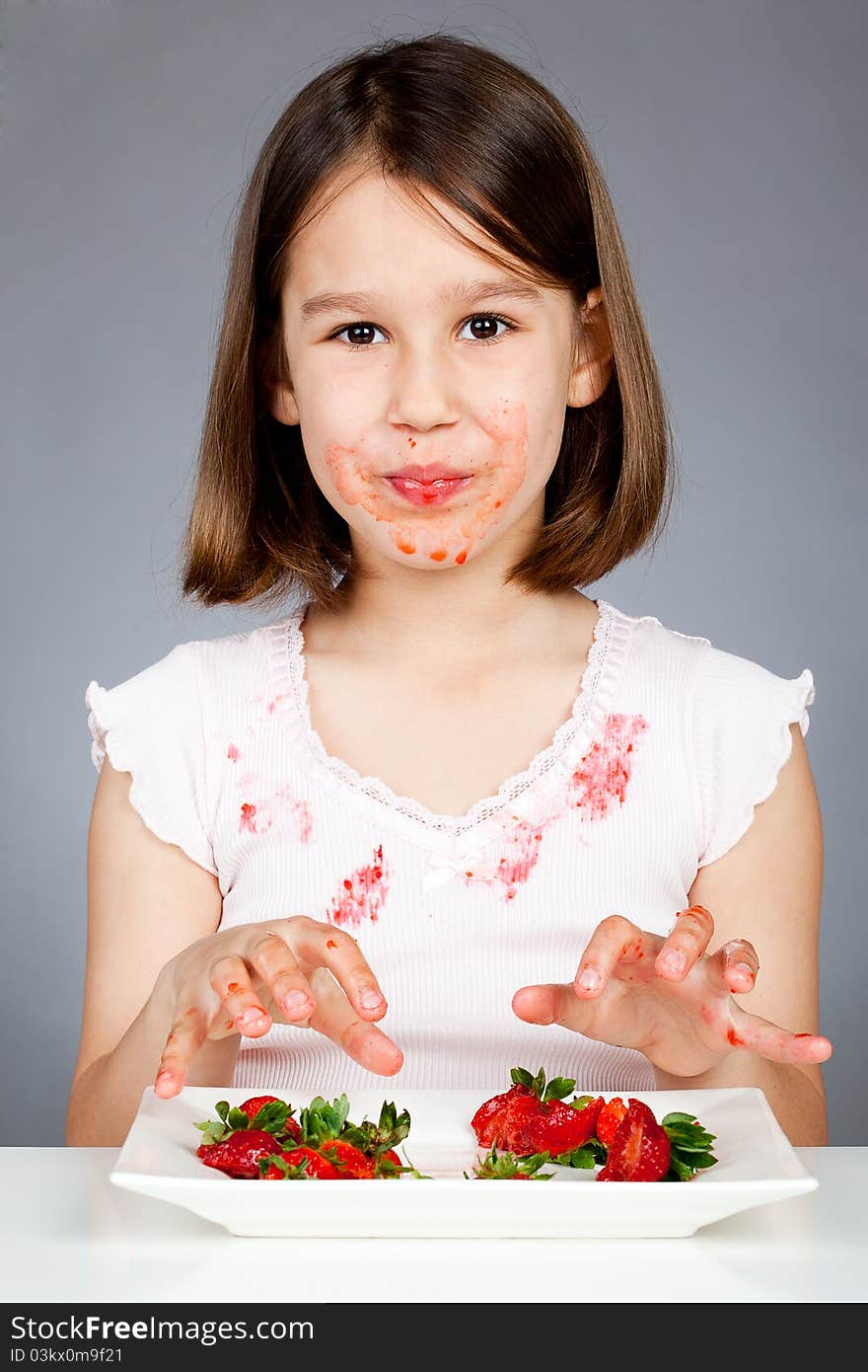 Portrait of cute little girl eating strawberries in the studio, grey background