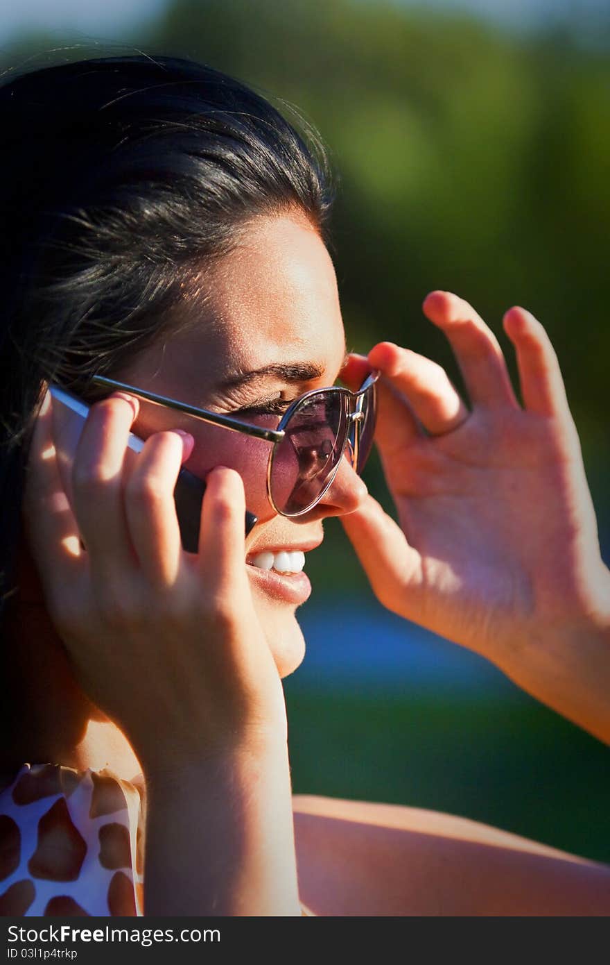 Portrait of a beautiful woman wearing sunglasses outdoors in the park talking on mobile phone. Portrait of a beautiful woman wearing sunglasses outdoors in the park talking on mobile phone