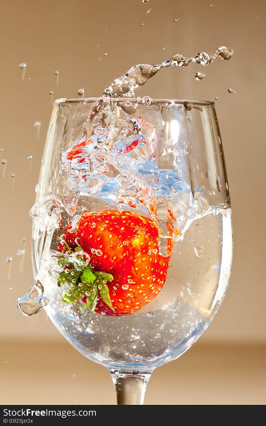 A single strawberry splashing in a glass of liquid.