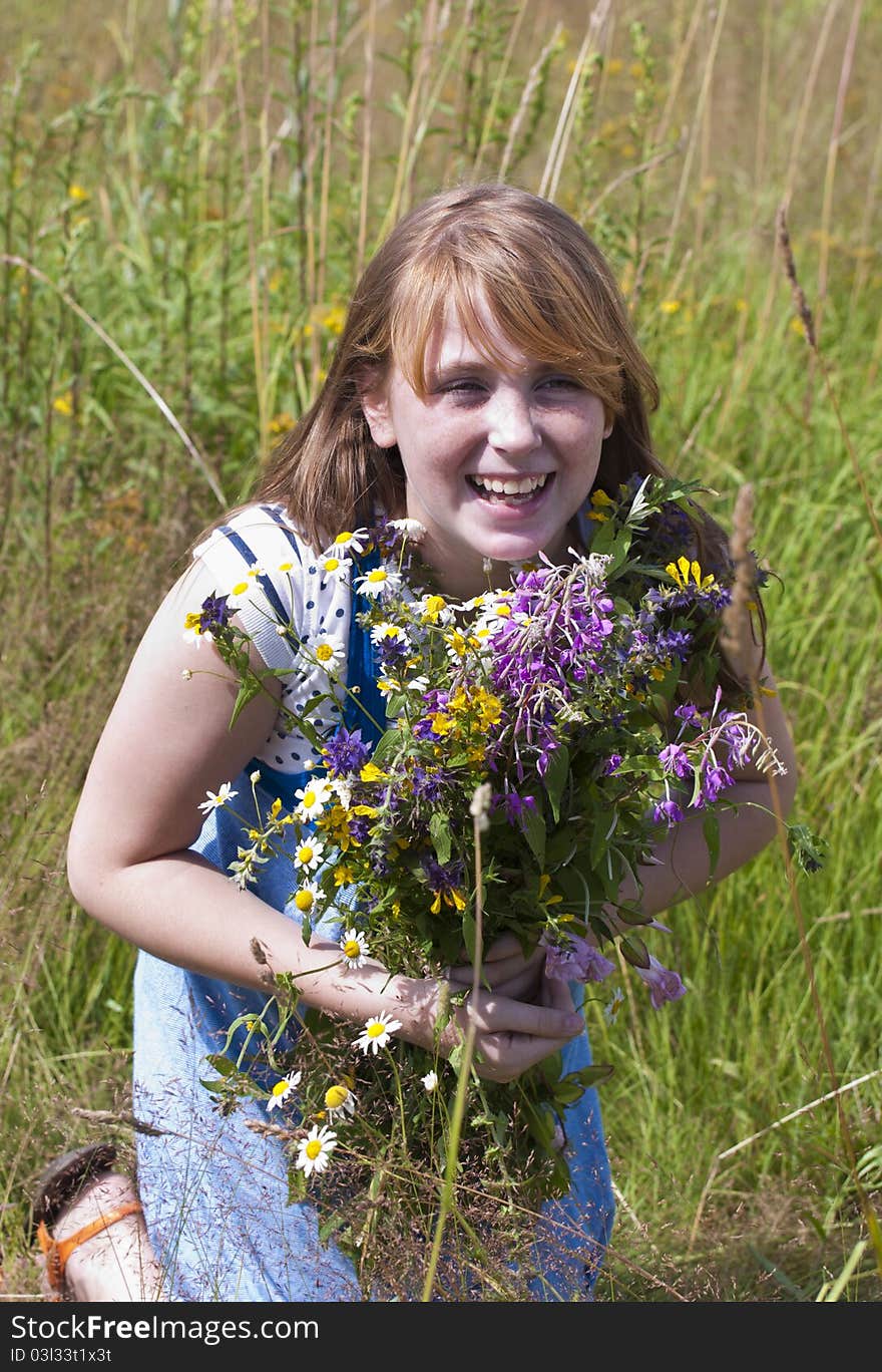 The happy red girl in the field with a bunch of flowers