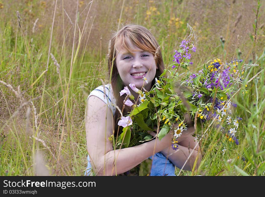 The smiling red girl in the field with a bouquet of flowers. The smiling red girl in the field with a bouquet of flowers