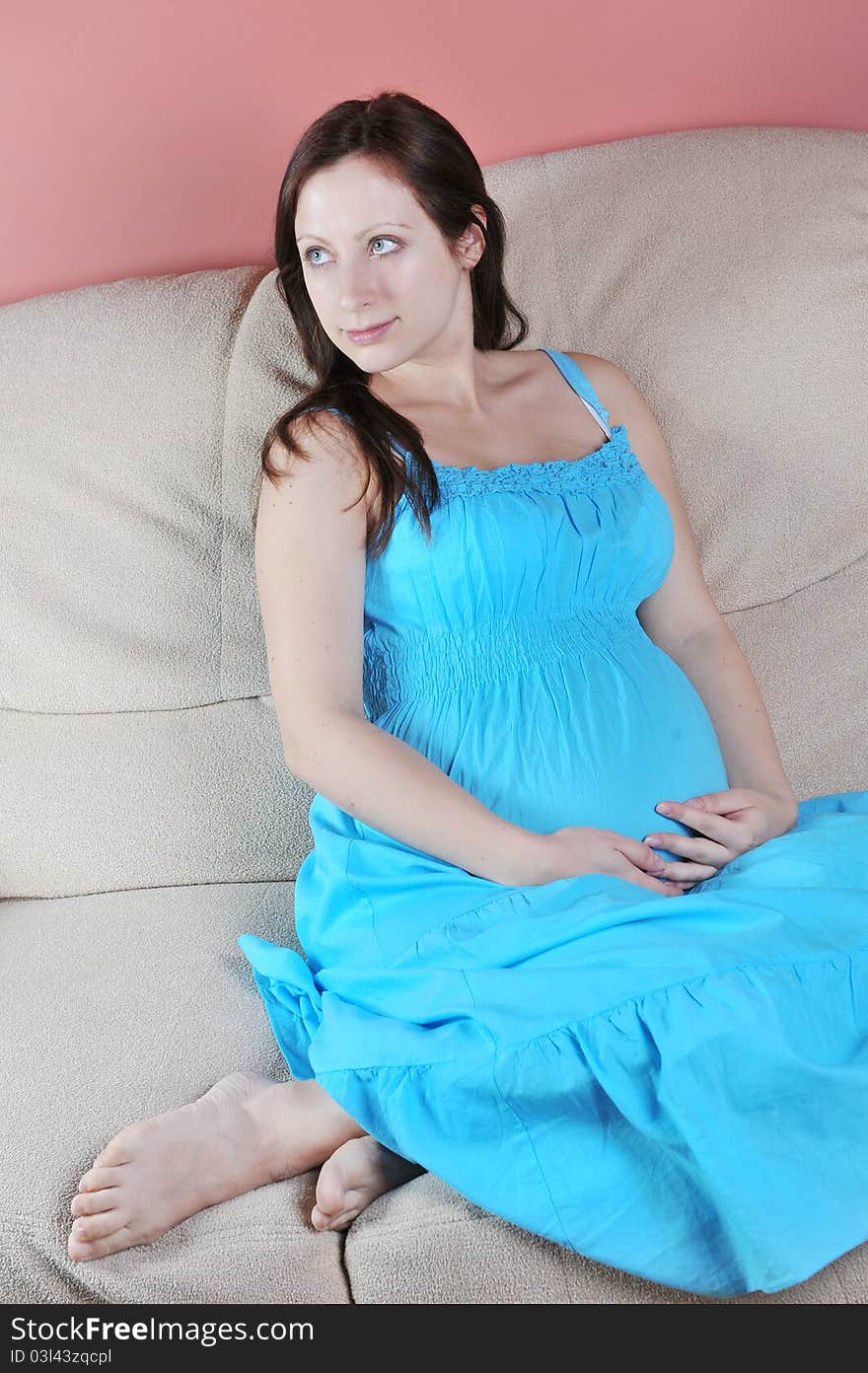 Pregnant woman in blue dress sitting on couch in living room. Pregnant woman in blue dress sitting on couch in living room