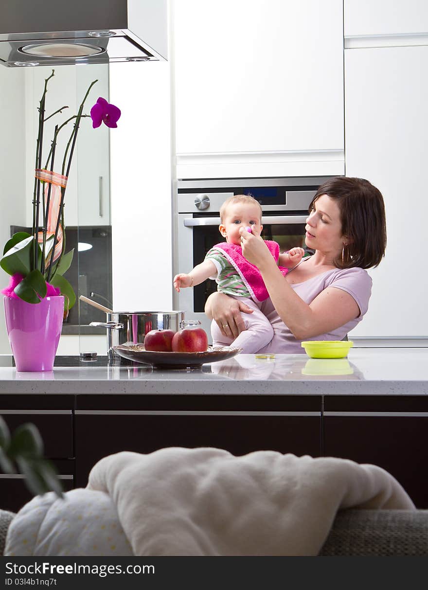 Young mother is feeding her baby in a modern kitchen setting. Young mother is feeding her baby in a modern kitchen setting.