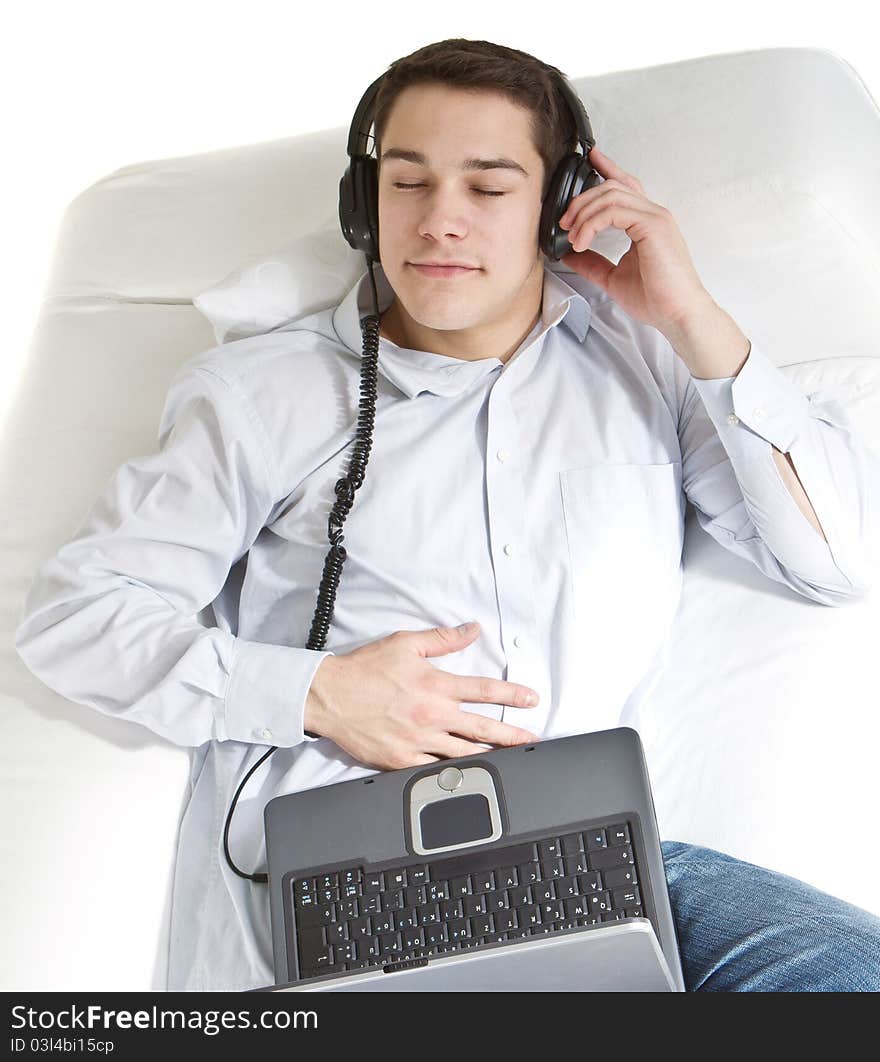 Young man relaxing on the couch listening to music over white background. Young man relaxing on the couch listening to music over white background.