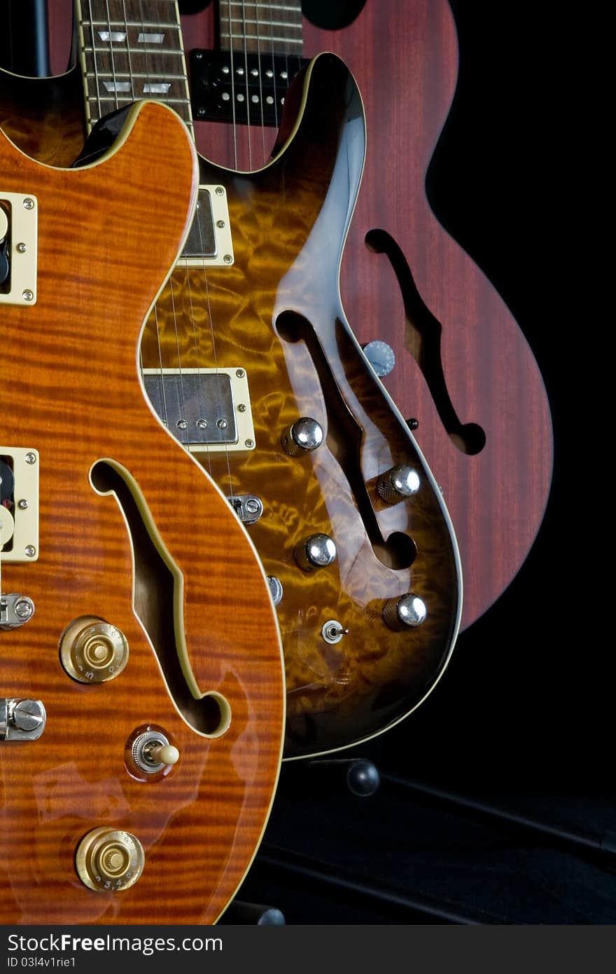 Three hollow body guitars on display with f holes on black background