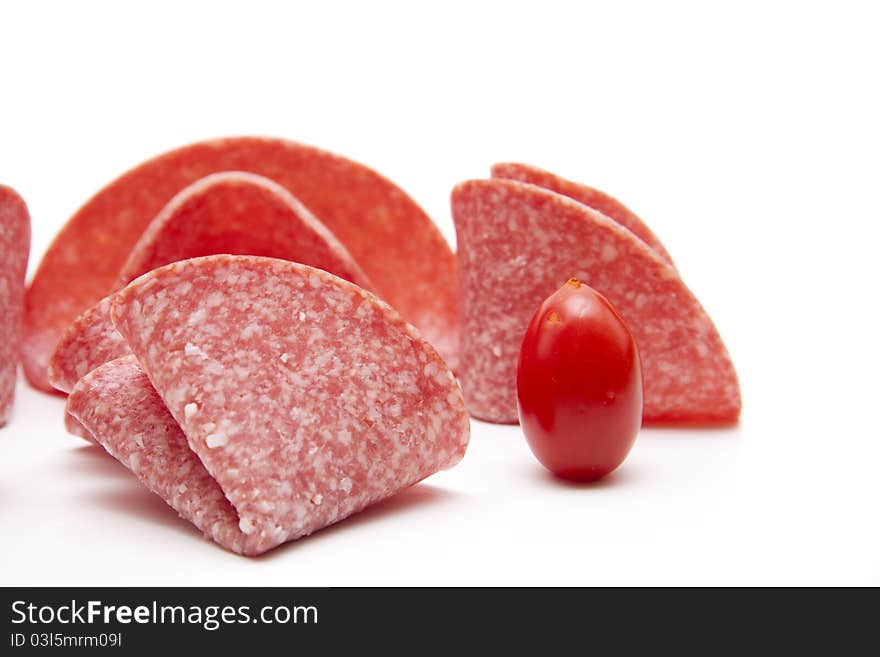 Salami folded with tomato onto white background