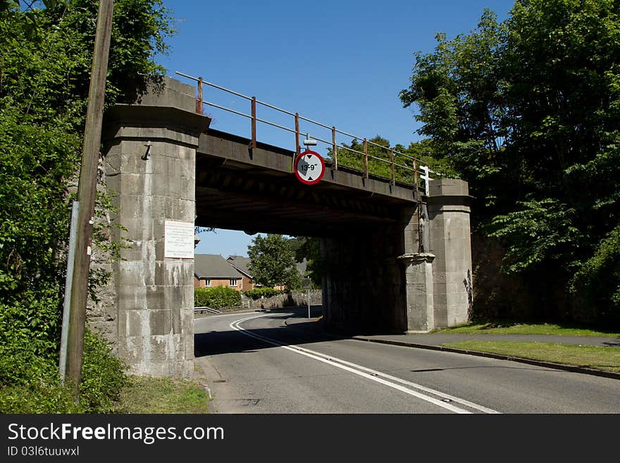 A low railway bridge built from stone with a railing and a sign giving the height of 13 feet and nine inches. A low railway bridge built from stone with a railing and a sign giving the height of 13 feet and nine inches.