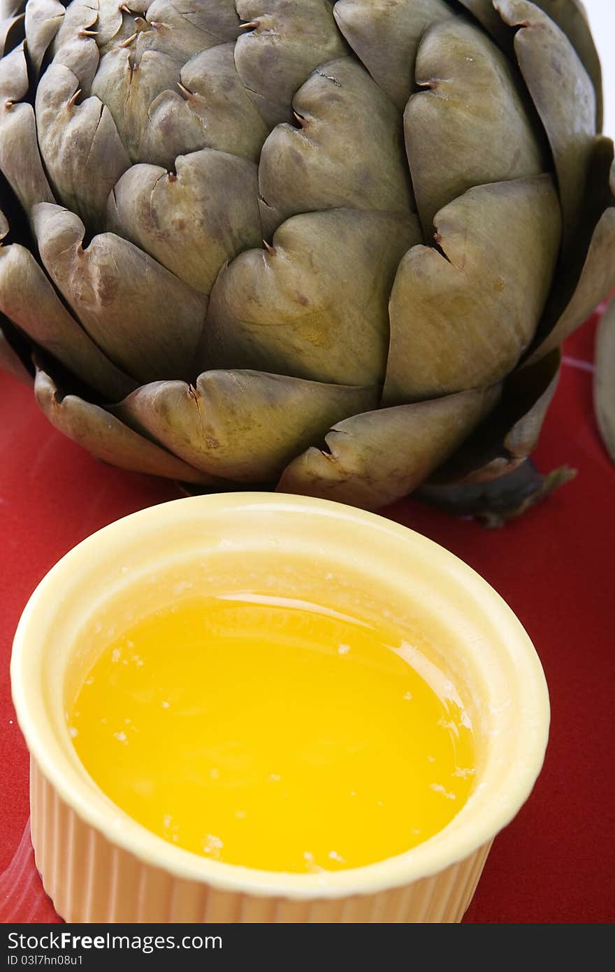 Steamed artichoke with melted butter on a red ceramic plate